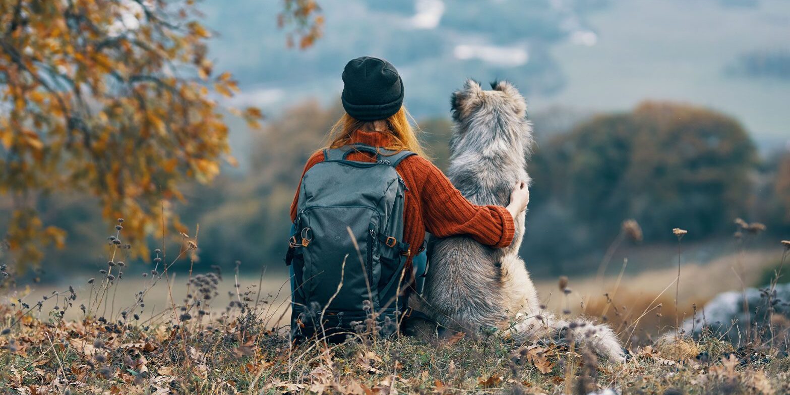 woman with red hair sitting with fluffy dog taking a break while hiking in mountains